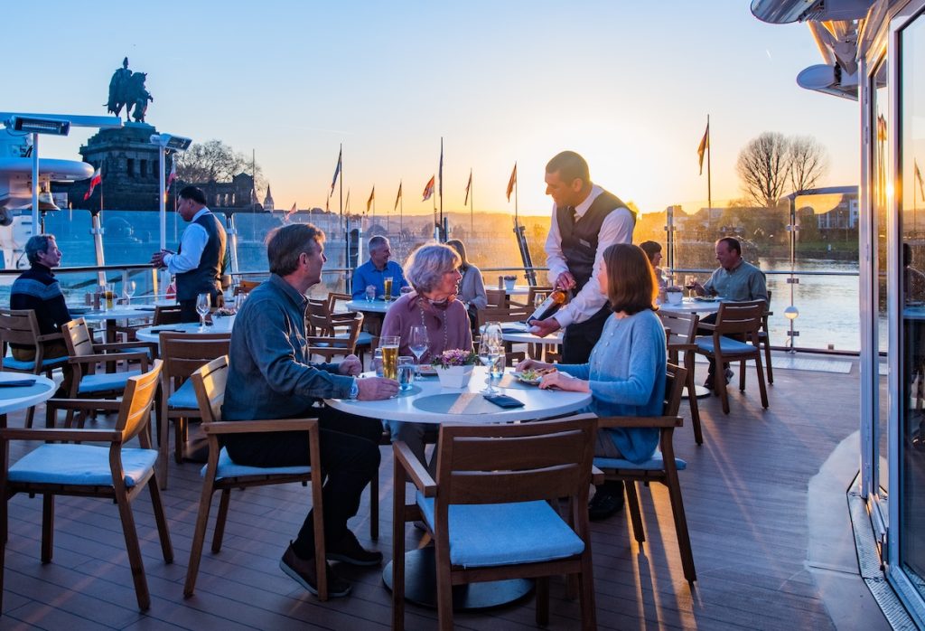Viking waiter serves wine to guests dining on the Aquavit Terrace at sundown on-board a Viking Longship, German Corner, Koblenz, Germany.